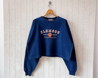 May include: A navy blue cropped sweatshirt with the text "CLEMSON GRANDPARENT" and an orange paw print.