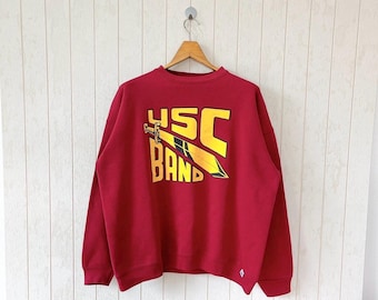 May include: Red sweatshirt with a yellow and black graphic of a sword and the text "USC Band".