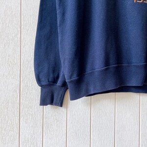 May include: A navy blue sweatshirt with ribbed cuffs and hem. The garment has a crew neck and appears to be made of a soft, comfortable material. The upper right corner of the sweatshirt has the partial text "195".