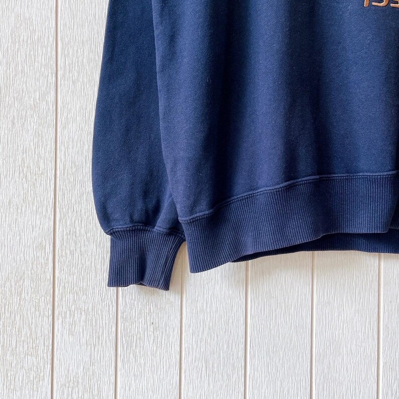 May include: A navy blue sweatshirt with ribbed cuffs and hem. The garment has a crew neck and appears to be made of a soft, comfortable material. The upper right corner of the sweatshirt has the partial text "195".