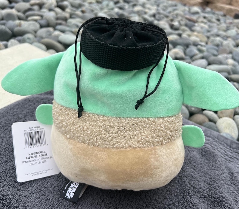 May include: A green and brown plush toy shaped like a character from Star Wars. The toy has a black drawstring bag on its head. The toy has a tag that says "Made in China. Fabriqu&eacute; en Chine. Mattel Canada Inc., Mississauga, Ontario, Canada L5N 3M2."