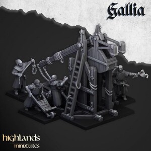 May include: A grey miniature trebuchet model with figures in medieval clothing. The model has a wooden frame, ropes, and a ladder. The word "Gallia" is at the top, and "highlands miniatures" is at the bottom.
