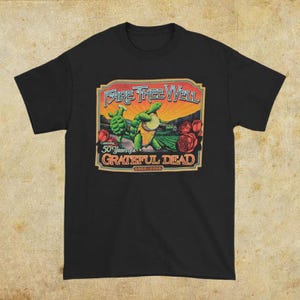 May include: Black t-shirt featuring a colorful graphic celebrating the Grateful Dead's 50th anniversary. The design includes two turtles, a sunset, roses, and the text "Fare Thee Well" and "50 Years of Grateful Dead 1965-2015".