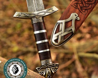 May include: A detailed image of a Viking sword with a patterned blade and a dark brown handle accented with silver bands. The hilt and pommel feature intricate metalwork. The wooden scabbard is visible, with a decorative metal piece and carved knotwork.