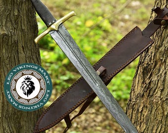 May include: A detailed image of a sword with a patterned blade and gold-colored crossguard. The sword rests in a brown leather sheath. The handle is black with a gold-colored pommel. The image includes a logo that says "Leo Vikings Mart".