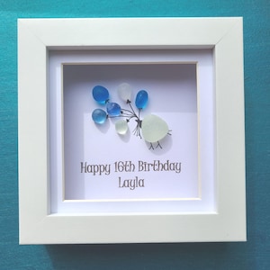 May include: White framed artwork with a birthday theme. The artwork features a cluster of blue and white glass balloons. The text "Happy 16th Birthday Layla" is printed below the balloons. The frame is square and white.