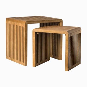 Puede incluir: Dos mesas nido de madera. Las mesas son de madera de color marrón claro y tienen un diseño de listones en la parte superior y los lados. Las mesas son cuadradas y tienen esquinas redondeadas. La mesa más grande es ligeramente más alta.
