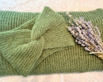 May include: A sage green knitted headband with a knotted design, resting on a matching knitted rectangle. A bundle of dried lavender tied with twine is placed on the right side. The headband is a stylish accessory.