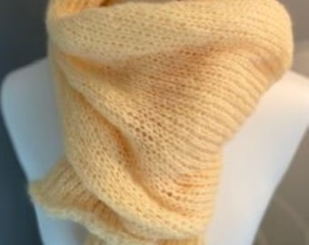 May include: A soft, pale yellow knitted scarf with a loose, airy texture. The scarf is wrapped around a white mannequin neck, featuring a ribbed pattern throughout the length of the fabric, creating a draped, layered appearance with visible stitches.