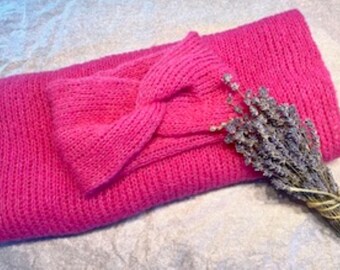 May include: A bright hot pink knitted headband featuring a central twist detail, paired with a matching hot pink knitted scarf. A small bundle of dried lavender tied with twine is positioned on the right side of the folded pink knit items.