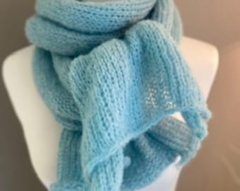 May include: A light blue knitted scarf with a loose, airy texture wrapped around a white mannequin. The scarf features a consistent ribbed stitch pattern throughout, with soft, fuzzy fibers visible across the entire length of the garment.