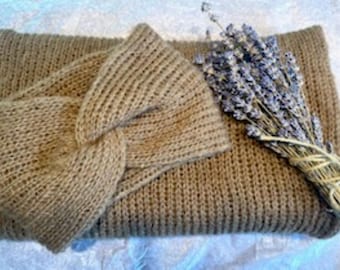 May include: A tan knitted headband with a central twist detail placed on top of a matching tan knitted scarf. A small bundle of dried purple lavender stems tied with twine is positioned across the right side of the scarf.