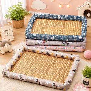 Puede incluir: Una cama rectangular para mascotas con un centro de esterilla de bambú tejida y bordes de tela acolchados. Los bordes están decorados con un patrón repetitivo de caras de gato estilizadas. La cama forma parte de una pila de esterillas similares.
