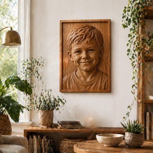 May include: A wooden relief carving of a smiling child's face, framed in a rectangular wooden border. The carving is mounted on a white wall, with natural light from a nearby window illuminating the details of the boy's hair and expression. The artwork is a portrait.