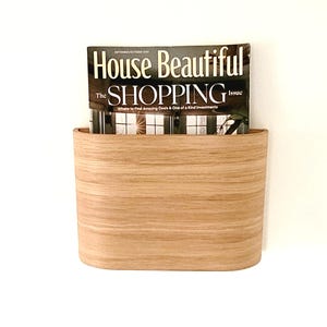 May include: A light wood magazine holder with a curved top and a magazine titled "House Beautiful The Shopping Issue" inside.