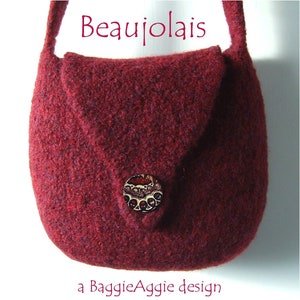 Puede incluir: Un bolso de mano de fieltro burdeos con cierre de solapa y un botón decorativo. El bolso tiene una correa corta y el texto "Beaujolais" está impreso encima del bolso. El texto "a BaggieAggie design" está impreso debajo del bolso.