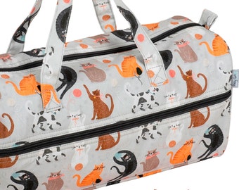 May include: A gray canvas zippered tote bag with a cat print design. The bag has two top handles and a zippered closure. The print features cats playing with yarn balls and other playful activities.