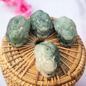 May include: Four jade green dragon pendants with intricate carvings, displayed on a woven basket.
