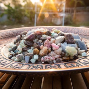 May include: A copper plate filled with a variety of colourful gemstones, including pink, blue, green, and brown. The gemstones are of various sizes and shapes, creating a visually appealing and textured display.