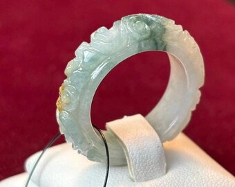 May include: A carved jade ring with a green and white color scheme. The ring is set on a white display stand.