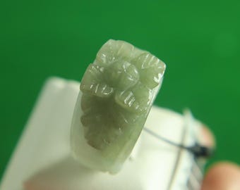 以下が含まれることがあります： 緑色の翡翠の指輪で、花柄が彫刻されています。指輪は白いディスプレイスタンドの上に置かれています。