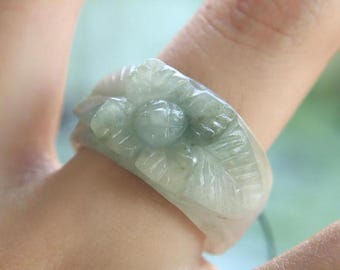 以下が含まれることがあります： 花柄が彫刻された翡翠の指輪。指輪は薄い緑色で、滑らかで磨かれた仕上げになっています。