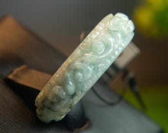 May include: A carved jade bangle with a delicate floral design. The bangle is a light green color and has a smooth, polished finish.