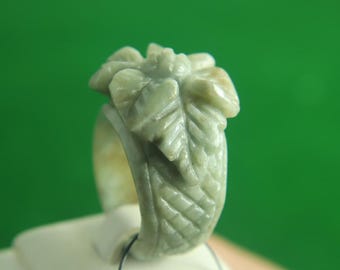 以下が含まれることがあります： 緑色の翡翠の指輪で、花柄が彫刻されています。指輪は滑らかで磨かれた石で作られており、繊細で複雑なデザインが施されています。