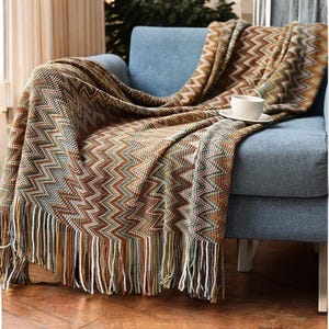 May include: A brown, beige and blue chevron patterned throw blanket with fringe on the edges. The blanket is draped over a blue armchair.