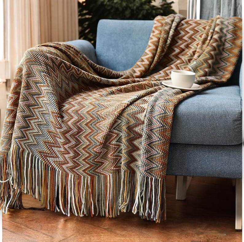 May include: A brown, beige and blue chevron patterned throw blanket with fringe on the edges. The blanket is draped over a blue armchair.