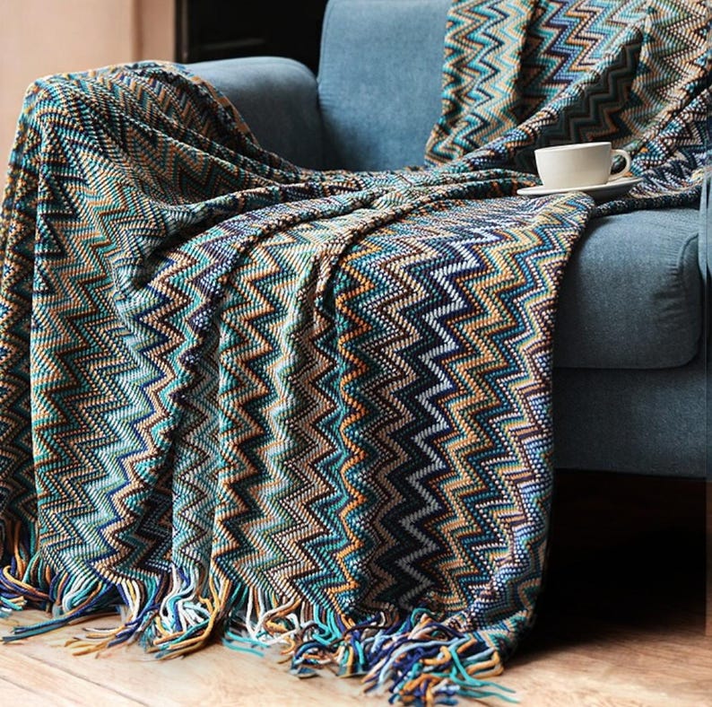 May include: A blue and brown chevron patterned throw blanket with fringe on the bottom edge. The blanket is draped over a blue armchair.