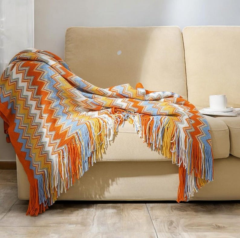 May include: A colourful throw blanket with a chevron pattern and fringe. The blanket is draped over a beige sofa.