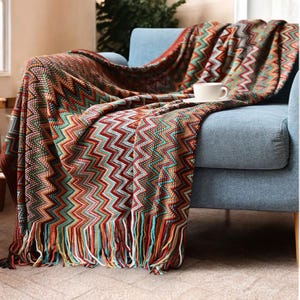 May include: A colourful throw blanket with a chevron pattern and fringe. The blanket is draped over a blue armchair.