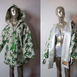 Op de afbeelding: Een witte gekapte robe met een groene marihuana-bladprint. De robe heeft een strik sluiting aan de hals en een satijnen voering.