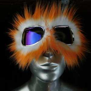 May include: Orange and white furry goggles with iridescent lenses. The goggles are worn on a mannequin's face.