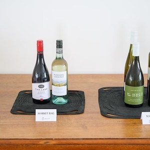 Puede incluir: Varias botellas de vino se exhiben sobre una mesa de madera. Las botellas están dispuestas sobre esteras negras, con pequeñas tarjetas delante. Las botellas tienen varias etiquetas y colores, incluyendo rojo, blanco y rosado.