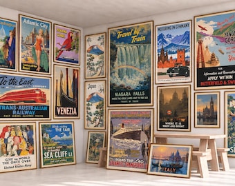 May include: A collection of vintage-style travel posters framed in light wood, displayed on walls and a wooden table. The posters feature various global destinations, including Niagara Falls, Italy, and the Trans-Australian Railway, with colorful illustrations and bold typography.