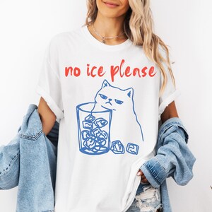 K&ouml;nnte beinhalten: Wei&szlig;es T-Shirt mit dem roten Text "no ice please". Eine blaue Strichzeichnung zeigt eine m&uuml;rrische Katze und ein Glas Eisw&uuml;rfel. Das T-Shirt ist ein l&auml;ssiger Unisex-Stil.
