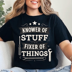 May include: Black t-shirt with the text "KNOWER OF STUFF FIXER OF THINGS" in white and gray. The design includes a star, a screwdriver, and a wrench. A fun gift for a handyman or anyone who likes to fix things.