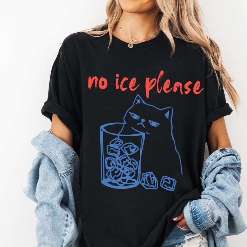 K&ouml;nnte beinhalten: Schwarzes T-Shirt mit dem roten Text "no ice please". Eine blaue Umrisszeichnung einer grummeligen Katze befindet sich neben einem Glas Eisw&uuml;rfel. Das T-Shirt hat einen l&auml;ssigen Stil.