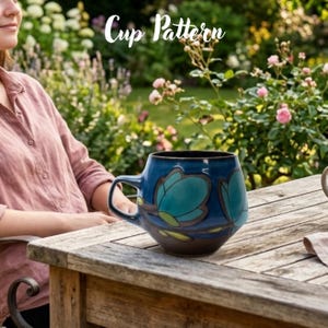 May include: A ceramic mug with a rounded body and a handle, featuring a dark blue and teal floral pattern with brown outlines. The text "Cup Pattern" is displayed in white script above the mug, which sits on a wooden surface.