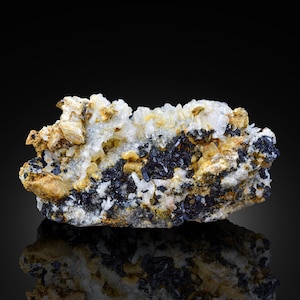Puede incluir: Un grupo de cristales negros brillantes incrustados en una matriz de roca blanca y marrón. Los cristales están rodeados de cristales más pequeños y transparentes.