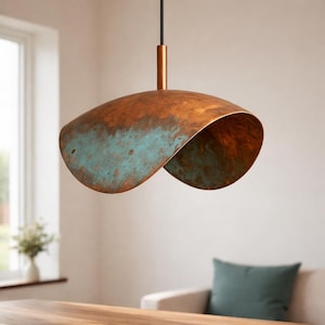 Peut inclure: Suspension luminaire en cuivre avec un design incurvé unique. La lampe présente un aspect vieilli avec des zones de patine bleu-vert. Elle est suspendue à un cordon noir et une tige de couleur cuivre.