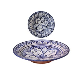 Peut inclure: Deux assiettes en céramique avec des motifs floraux bleus et blancs complexes. La plus grande est ovale, la plus petite ronde. Les deux assiettes présentent un motif détaillé sur les bords et un motif floral central, d'esthétique traditionnelle.