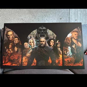 Op de afbeelding: Een rechthoekige poster met personages uit een fantasieserie. Het kunstwerk toont een centrale figuur met lang wit haar, omringd door andere personages. De achtergrond is donker met oranje en rode tinten.