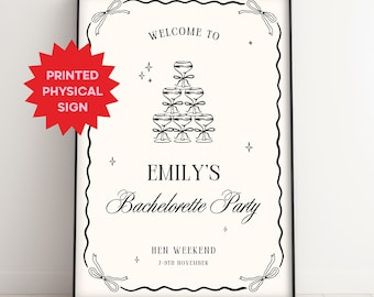 Puede incluir: Un letrero enmarcado con un borde negro y un fondo color crema. El letrero dice "WELCOME TO EMILY'S Bachelorette Party" con una ilustración de pirámide de copas de champán. También está presente el texto "HEN WEEKEND 7-9TH NOVEMBER". Una etiqueta roja en forma de estrella dice "PRINTED PHYSICAL SIGN".