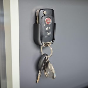 Könnte beinhalten: Ein schwarzer Schlüsselanhänger mit einem roten FIAT-Logo und vier Knöpfen. Der Schlüsselanhänger ist an einem silbernen Schlüsselring mit zwei zusätzlichen Schlüsseln befestigt.