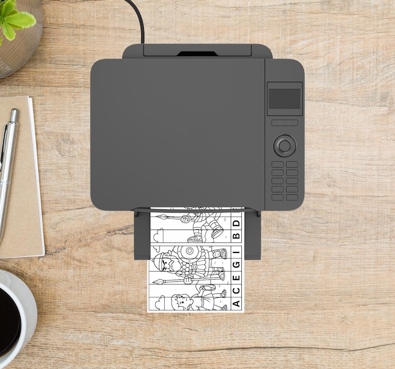 May include: A gray printer is printing a black and white puzzle featuring cartoon illustrations of Roman soldiers. The puzzle pieces are labeled with letters. The printer sits on a wooden surface, with a pen and notepad visible.