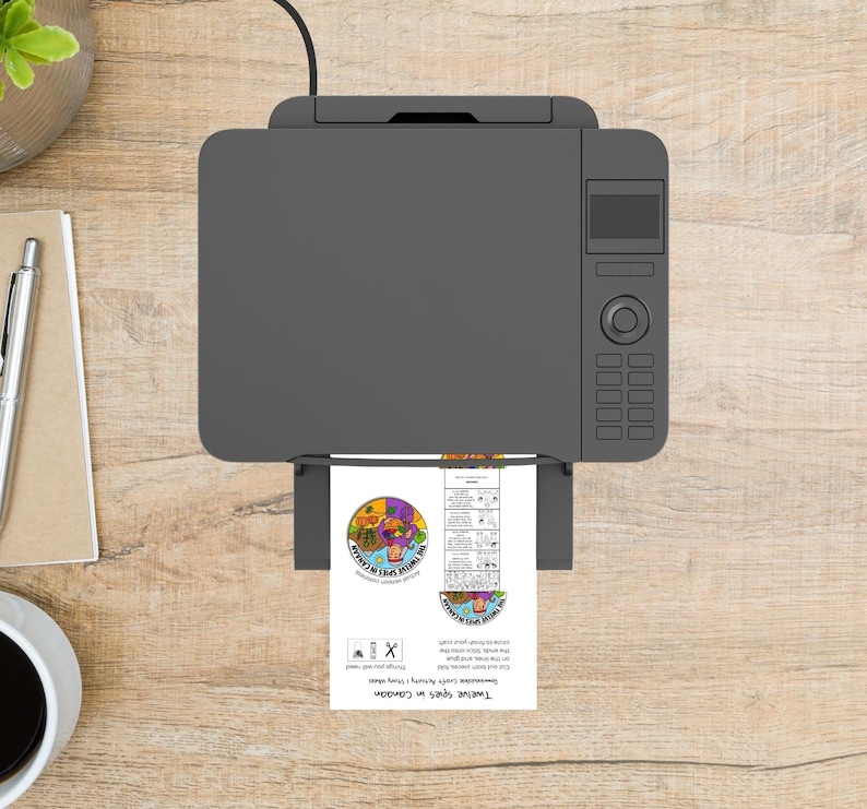 May include: A gray printer is printing a document with colorful graphics and text. The document features a circular design with various images and the text "Twelve Spies in Canaan". The printer sits on a wooden surface.