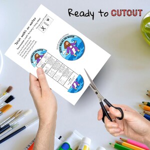 May include: A white paper craft activity sheet titled "Jesus walks on water" with a colorful illustration of Jesus walking on water. The sheet includes instructions and is being cut with scissors. The text "Ready to CUTOUT" is at the top.